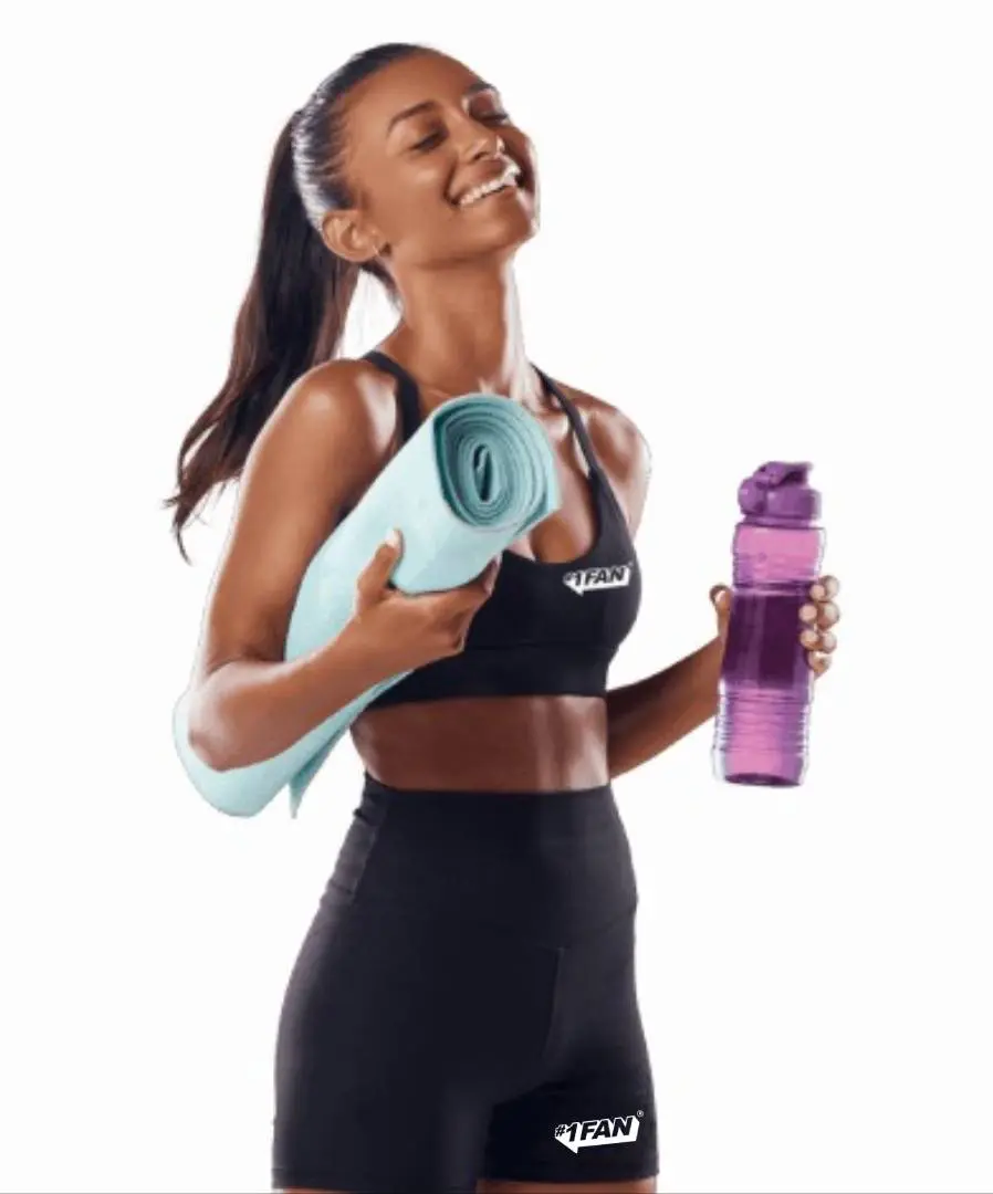 Woman in workout clothes holding a yoga mat and water bottle, smiling.