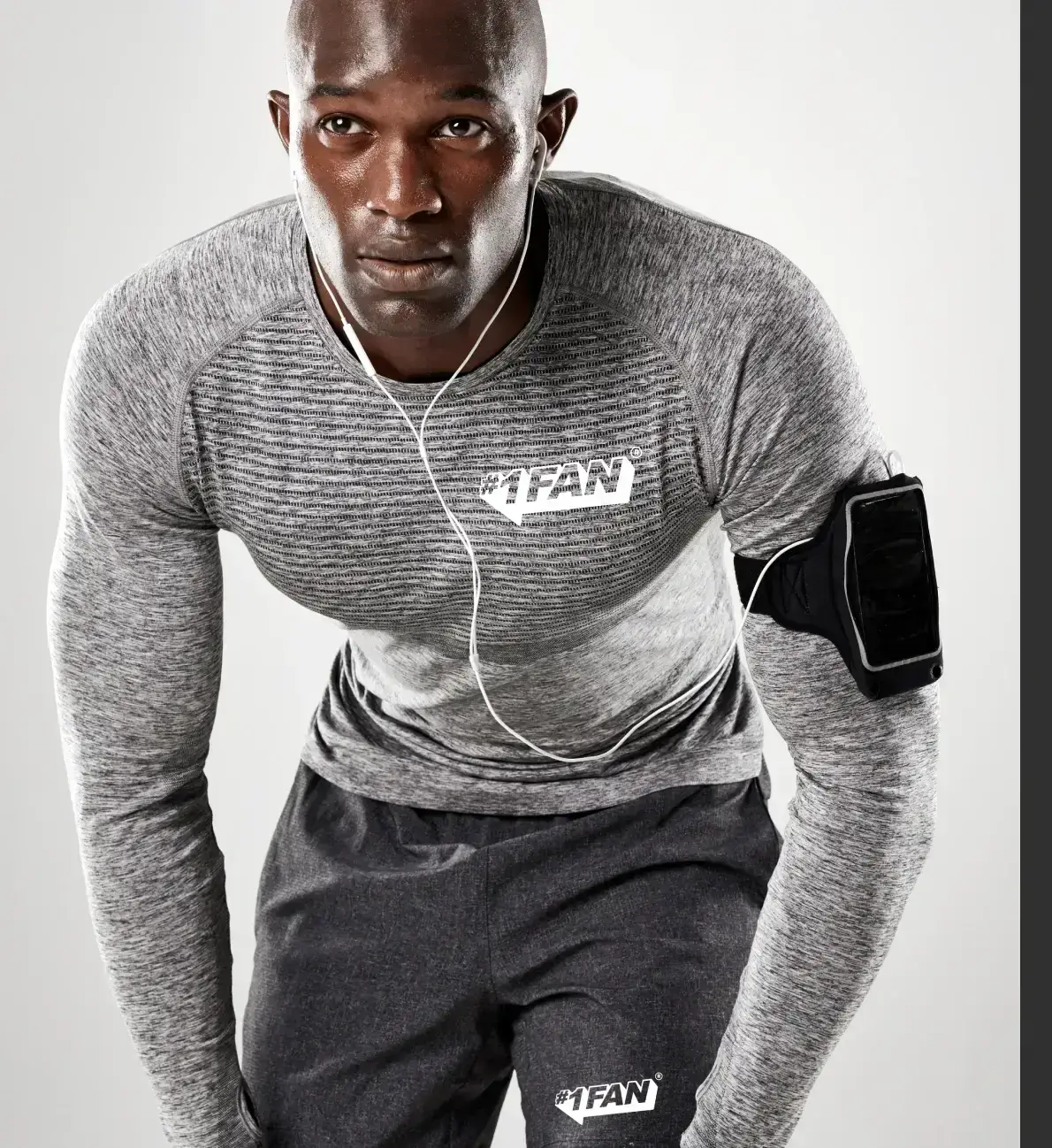 Athletic man in gray workout gear with earphones and arm phone holder.